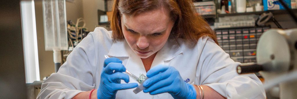 female student with red hair, white lab coat and blue latex gloves conducting research