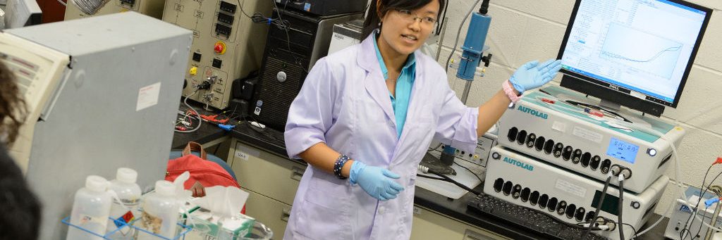 oriental female with glasses, white lab coat with blue latex gloves in front of a computer making a presentation