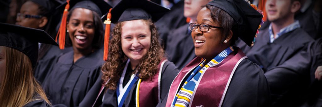 three seated females in commencement regalia smiling with one another celebrating their commencement
